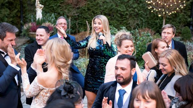 Hochzeit: Christoph (Dieter Bach), Alicia (Larissa Marolt) und die Hochzeitsgäste genießen den Auftritt von Schlagerstar Beatrice Egli (h.) in vollen Zügen.