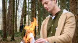 Joshua (Julian Schneider, h.) beobachtet, wie Henry (Patrick Dollmann, vorne) im Wald Dokumente verbrennt.