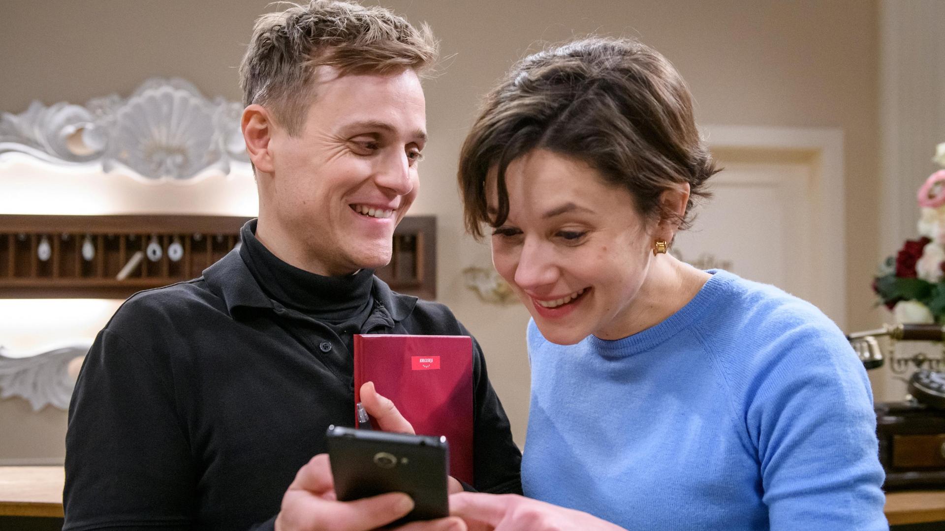 Max (Stefan Hartmann) zeigt Eleni (Dorothée Neff) stolz Bilder von Arthur.