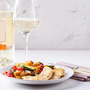 Ein Teller mit Hühnchenfleisch und gegrilltem Gemüse und ein Glas Weißwein - Tipps für Wein zum Grillen