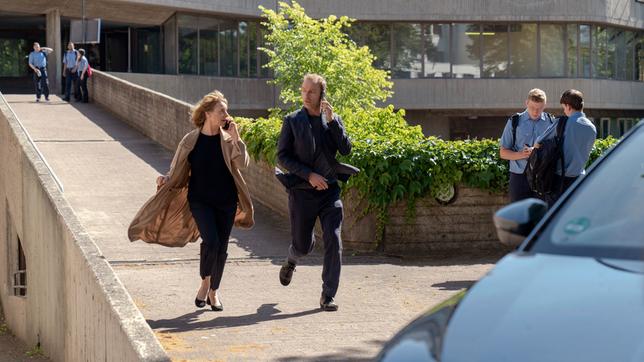 Bild: rbb/Marcus Glahn Kommissarin Susanne Bonard (Corinna Harfouch) und Kommissar Robert Karow (Mark Waschke) eilen vor der Polizeiakademie zu ihrem Auto, sie haben wichtige Informationen per Telefon erhalten.